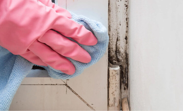 Gloved hand wiping a discolored window or door track.